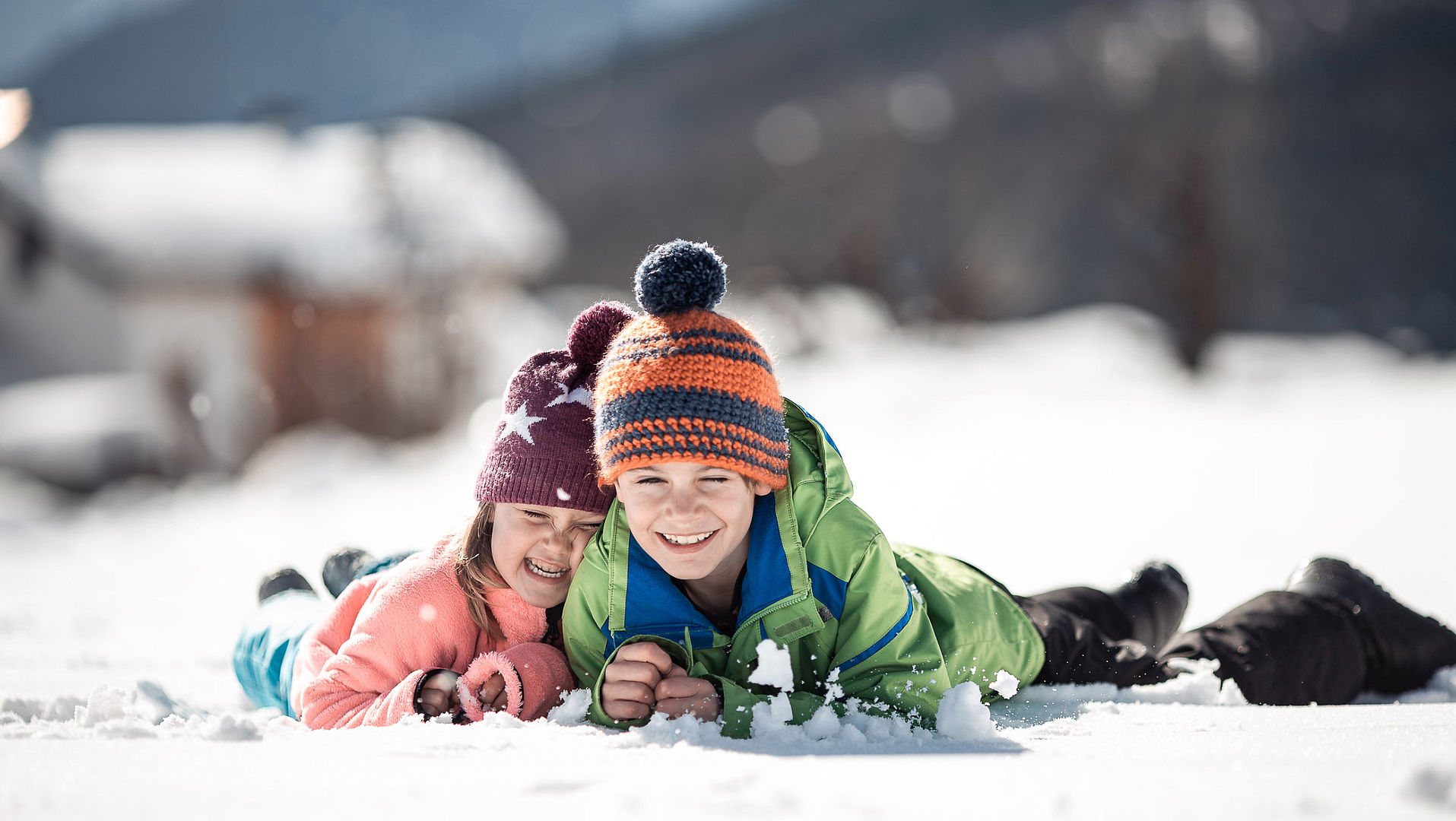 Zwei Kinder liegen auf dem Bauch im Schnee und umarmen sich