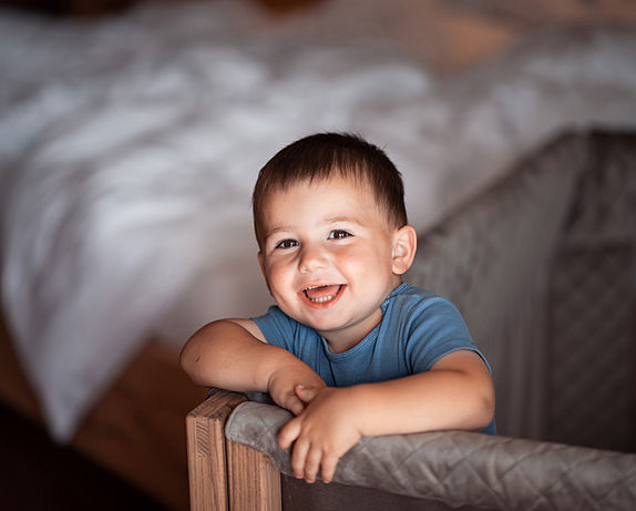Toddler stands in the baby cot and smiles