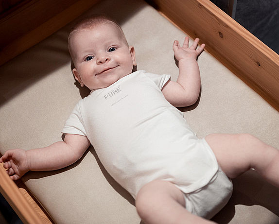 Baby with white bodysuit in the cradle
