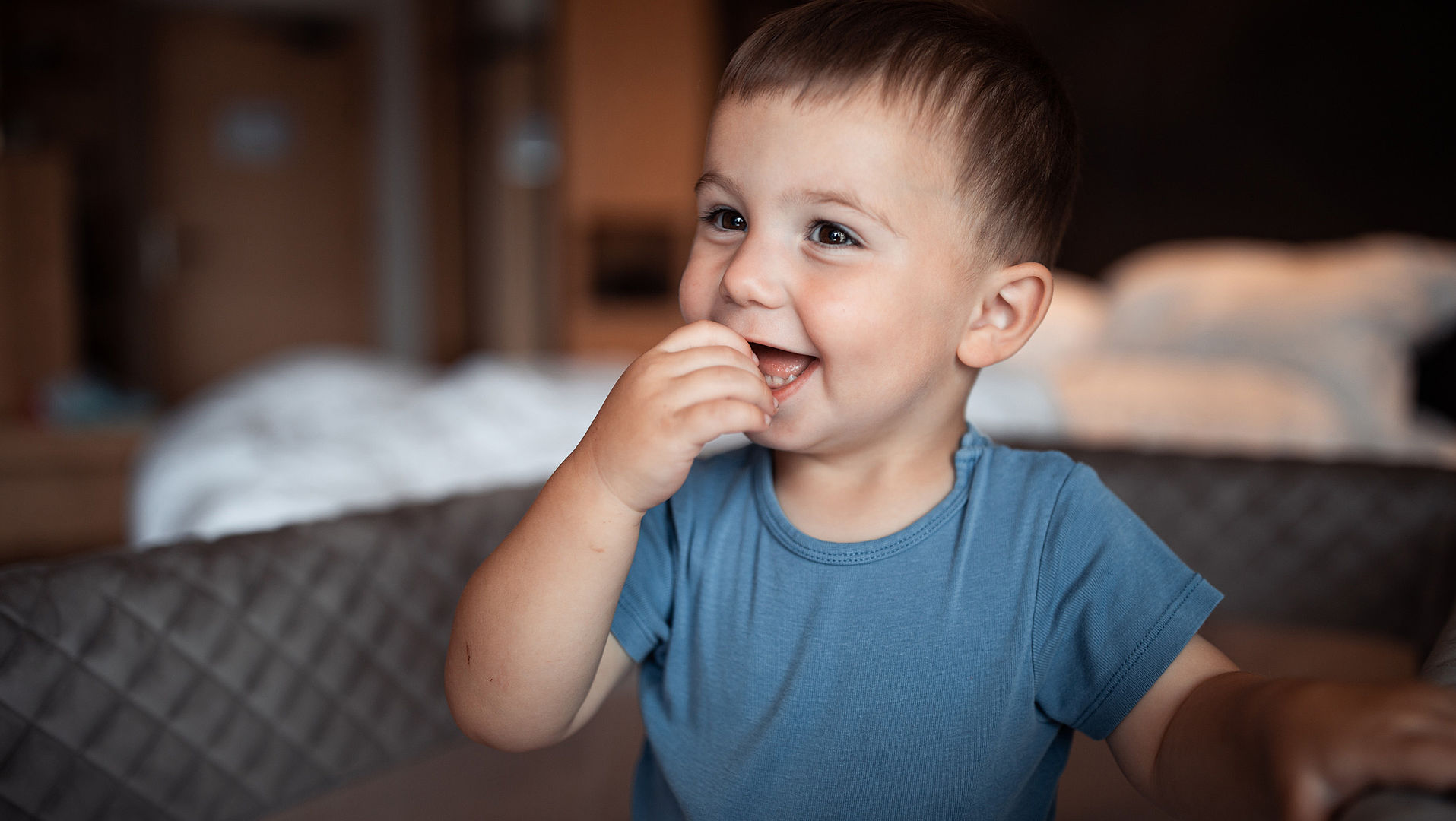 Toddler with blue T-shirt laughing in bed