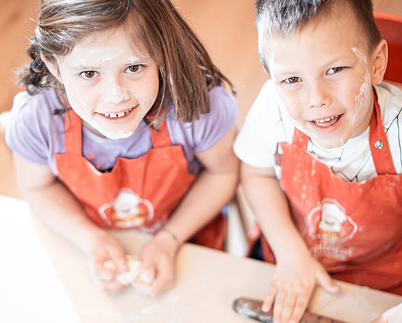 Children with flour on their faces help with kneading