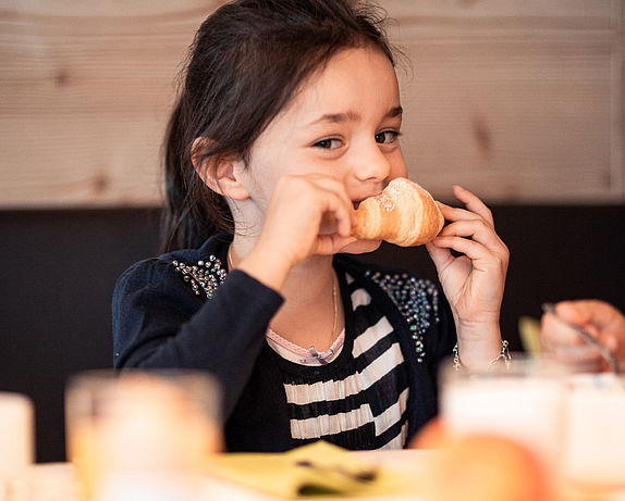 Bambina che mangia un croissant a colazione